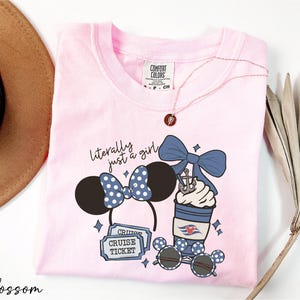 A pink t-shirt with a graphic design featuring a pair of Minnie Mouse ears, a cup of ice cream, sunglasses, and a cruise ticket, along with the text "Literally just a girl" and "Cruise Ticket".