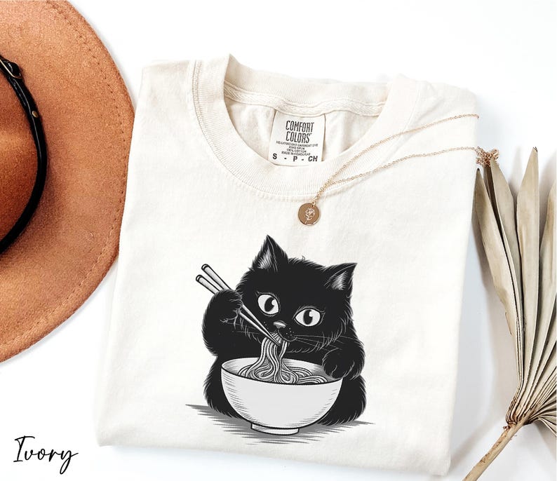 A white t-shirt with a black cat illustration and the word "Ivy" printed on it, along with a necklace and a hat.