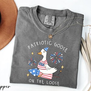 a patriotic goose on the loose t - shirt next to a hat