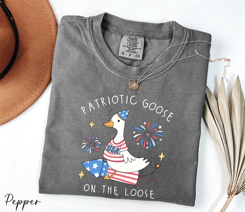 a patriotic goose on the loose t - shirt next to a hat