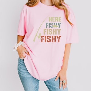 a woman wearing a pink shirt that says, here fishy fishy fishy