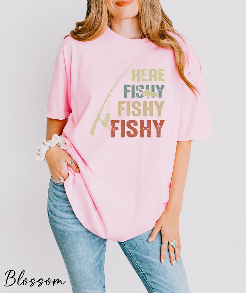 a woman wearing a pink shirt that says, here fishy fishy fishy