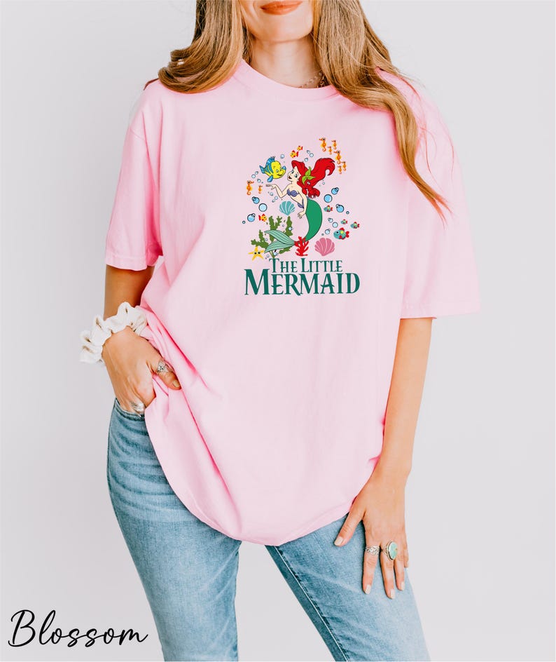 a woman wearing a pink shirt with the words the little mermaid on it
