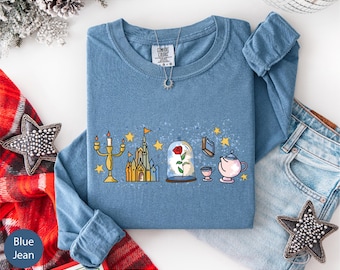 May include: Blue jean long-sleeve shirt with a graphic featuring a candelabra, castle, rose in a glass dome, book, teacup, teapot, and stars. The shirt has a crew neck and a tag that says "Comfort Colors".