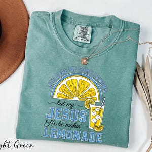 A light green t-shirt with a graphic design and text, along with a brown hat and some dried leaves, on a white background.