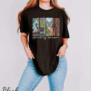 A woman wearing a black t-shirt with a graphic design depicting various hunting animals, including a deer, duck, and bear, along with the text "Hunting Season".