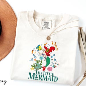 a hat, sunglasses, and t - shirt with the little mermaid on it
