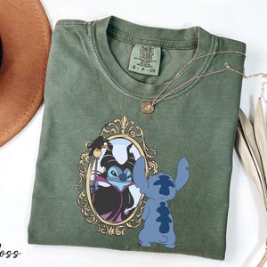 A green t-shirt with a design featuring a character from the Disney movie "Stitch" and a mirror, along with a necklace and a hat.