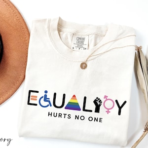 May include: Ivory t-shirt with the text "EQUALITY HURTS NO ONE" in black. The word "EQUALITY" is made up of various symbols including a wheelchair, a rainbow triangle, a raised fist, and a gender symbol.