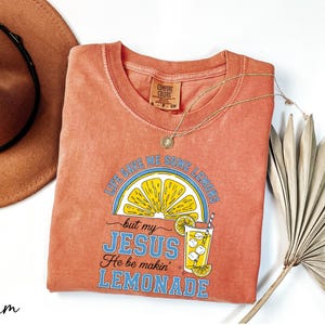 a red t-shirt with a graphic design, a brown hat, a necklace, and a fan, all laid out on a white background.