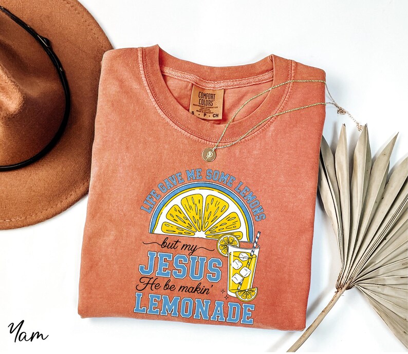 a red t-shirt with a graphic design, a brown hat, a necklace, and a fan, all laid out on a white background.