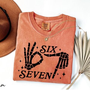 a pink t-shirt with a graphic design, a brown hat, a necklace, and a fan, all arranged on a white background.
