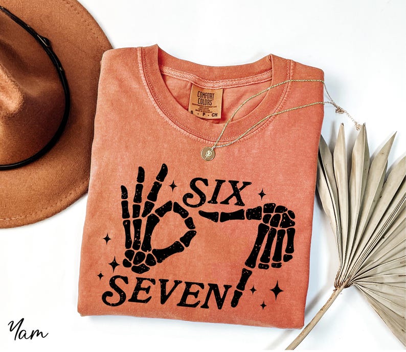 a pink t-shirt with a graphic design, a brown hat, a necklace, and a fan, all arranged on a white background.