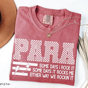 a red t-shirt with a white text design, a brown hat, and some dried leaves, all placed on a white surface.
