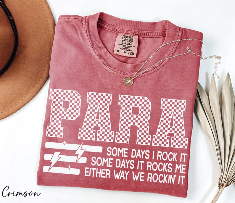a red t-shirt with a white text design, a brown hat, and some dried leaves, all placed on a white surface.