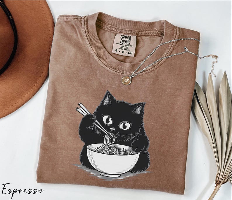 a brown t-shirt with a black cat graphic, holding a bowl of noodles and eating with chopsticks.