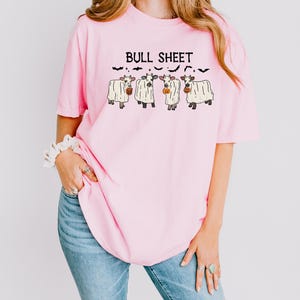 A woman wearing a pink t-shirt with a graphic design of four cows and the text "Bull Sheet" printed on it.