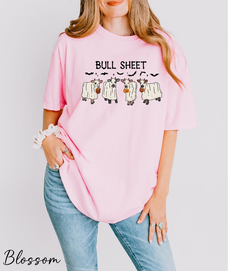 A woman wearing a pink t-shirt with a graphic design of four cows and the text "Bull Sheet" printed on it.