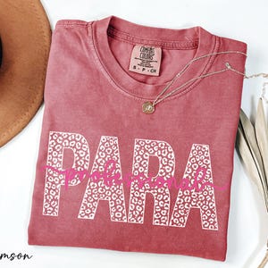 a pink t-shirt with the word "PARA" printed on it, along with a necklace and a hat.