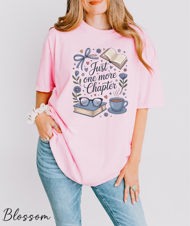 A woman wearing a pink t-shirt with a graphic design featuring a book, glasses, and a cup of coffee, along with the text "Just one more Chapter".