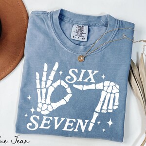 A blue t-shirt with a white graphic design, a necklace, a hat, and some dried leaves on a white background.