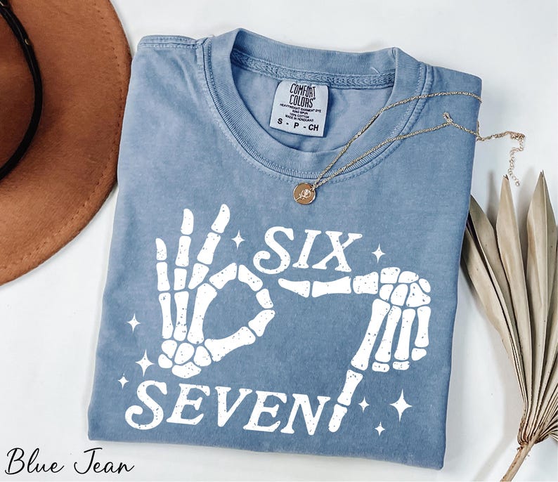 A blue t-shirt with a white graphic design, a necklace, a hat, and some dried leaves on a white background.