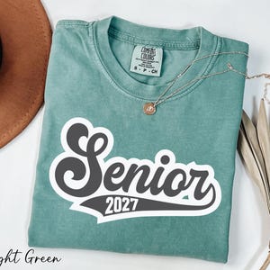 A light green t-shirt with a black and white text design that says "Senior 2027" is displayed on a white background.