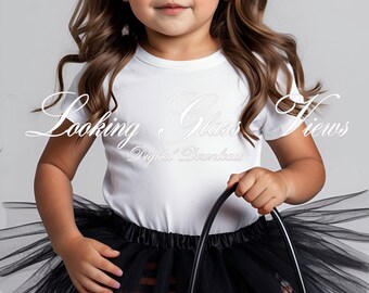 Può includere: Una bambina vestita con una gonna di tulle nera, leggings a righe arancioni e nere e una maglietta bianca con la scritta "Looking Glass Views Digital Downloads" stampata su di essa. La bambina indossa occhiali da sole neri a forma di occhio di gatto e una fascia per capelli nera con paillettes e un fiocco. La bambina tiene un secchiello arancione a forma di zucca per dolcetto o scherzetto.