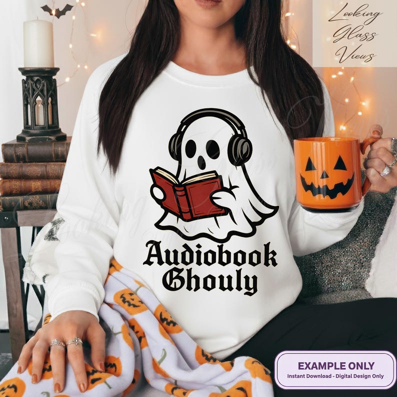 Pode incluir: Camisola branca com um desenho de um fantasma a usar auscultadores e a ler um livro. O texto "Audiobook Ghoul" est&aacute; por baixo. Uma caneca laranja em forma de ab&oacute;bora &eacute; segurada na m&atilde;o. O tema &eacute; o Halloween.