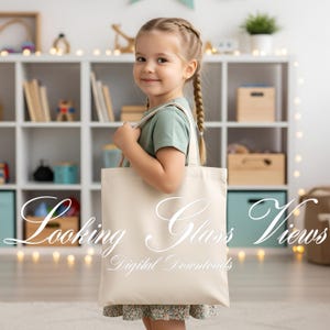 May include: A young girl holds a cream-colored tote bag with the words "Looking Glass Views Digital Downloads" in elegant script. The bag has long straps and appears to be made of canvas. The girl is wearing a green shirt and a floral skirt.