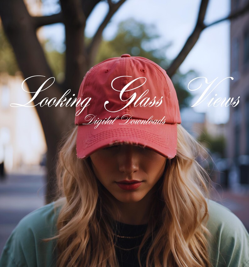 May include: A woman wearing a red baseball cap with the text "Looking Glass Views Digital Downloads" on it. She has long blonde hair and is looking down.