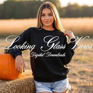 May include: A person wearing a black crew neck sweatshirt and denim shorts, leaning on a hay bale next to a large orange pumpkin. The sweatshirt has the text "Looking Glass Views Digital Downloads" in white script.
