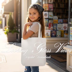 Puede incluir: Una persona sonr&iacute;e mientras sostiene una bolsa de mano blanca con el texto "Looking Glass Views Digital Downloads". La persona lleva un pa&ntilde;uelo negro, una camiseta beige y vaqueros azules. El fondo muestra una librer&iacute;a.