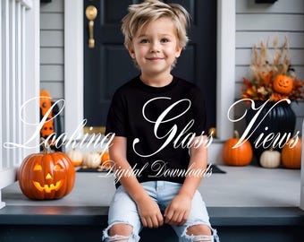 Può includere: Un bambino con una maglietta nera e jeans strappati è seduto su un portico. La maglietta ha la scritta "Looking Glass Views" in corsivo bianco. Zucca intagliata e altre zucche suggeriscono un tema di Halloween.