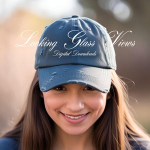 May include: A blue distressed baseball cap with the text "Looking Glass Views" and "Digital Downloads" in white. The cap is worn by a person with long brown hair.