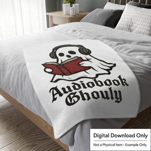 Pode incluir: Cobertor branco com um fantasma de desenho animado usando fones de ouvido e lendo um livro vermelho. O texto "Audiobook Ghoul" &eacute; impresso em letras g&oacute;ticas pretas. O cobertor est&aacute; em uma cama com roupa de cama branca.