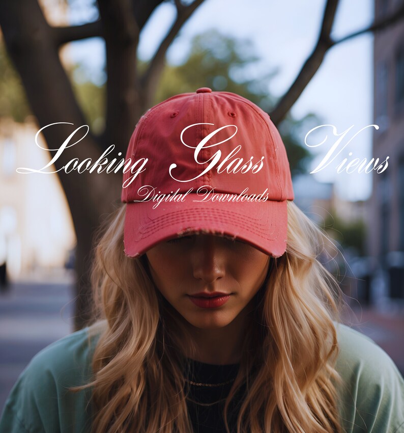 May include: A woman wearing a red baseball cap with the text "Looking Glass Views Digital Downloads" on it. She is looking down with her blonde hair covering her eyes.