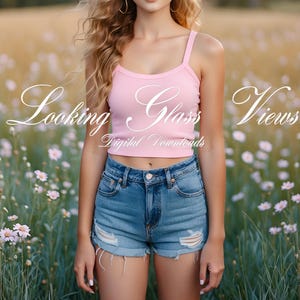 May include: A woman wearing a pink tank top with the text "Looking Glass Views" and blue denim shorts stands in a field of wildflowers.