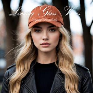 May include: A woman with long blonde hair is wearing a brown baseball cap with the text "Looking Glass" and "Digital Downloads" on it. She is also wearing a black leather jacket.