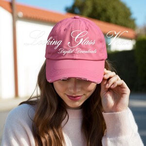 May include: A pink distressed baseball cap with the text "Looking Glass Views Digital Downloads" in white.