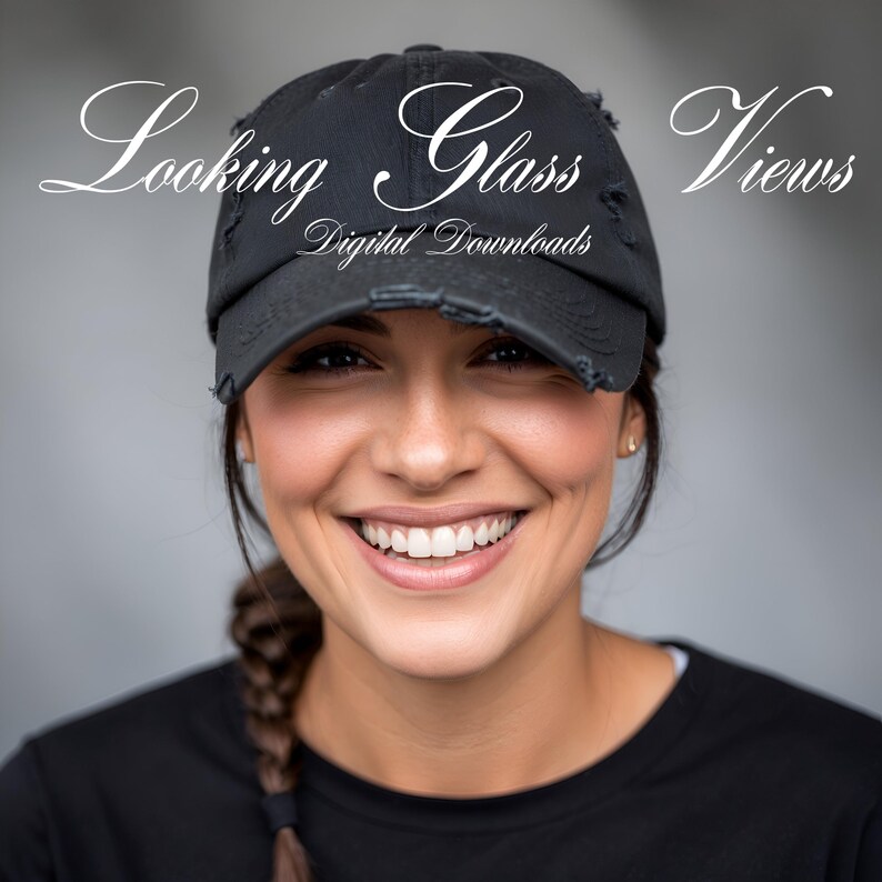 May include: A woman with a bright smile is wearing a black baseball cap with the text "Looking Glass Views Digital Downloads" on it. She is wearing a black shirt and has a braid in her hair.