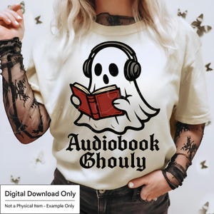 Pode incluir: Camiseta creme com um desenho de um fantasma usando fones de ouvido e lendo um livro vermelho. O texto "Audiobook Ghoul" est&aacute; impresso abaixo do fantasma em uma fonte g&oacute;tica. A camiseta &eacute; um download digital.