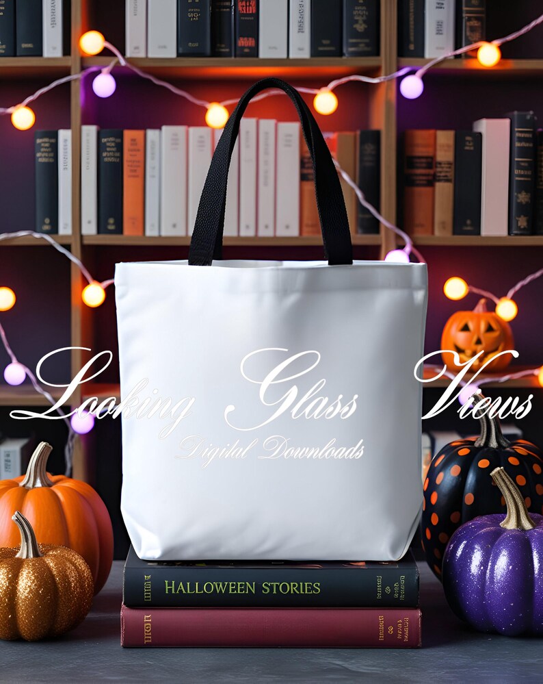 May include: White tote bag with black handles, featuring the text "Looking Glass Views Digital Downloads". The bag is sitting on a stack of books with the title "Halloween Stories" visible. The bag is surrounded by decorative pumpkins.