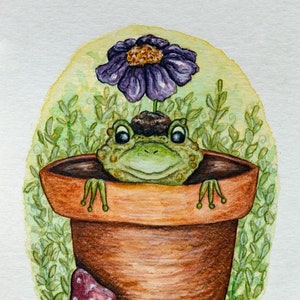 May include: Watercolor painting of a cheerful frog in a terracotta pot, with a purple flower sprouting from its head. Two red mushrooms with white spots sit at the base of the pot, set against a green background.