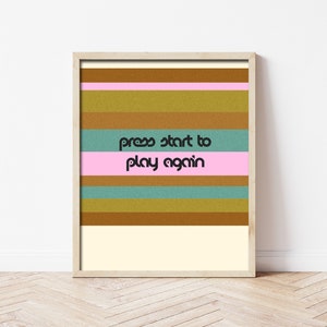 May include: A digital art print with a retro design featuring horizontal stripes in shades of brown, pink, and blue. The text "press start to play again" is centered on the print.