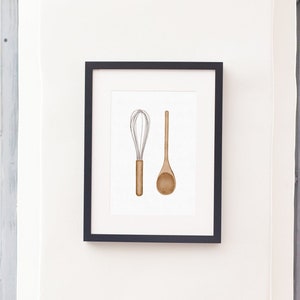 May include: Framed print featuring a watercolor illustration of a whisk and a wooden spoon. The whisk has a brown handle and silver wires. The spoon is light brown. The artwork is displayed in a black frame, perfect for kitchen decor.