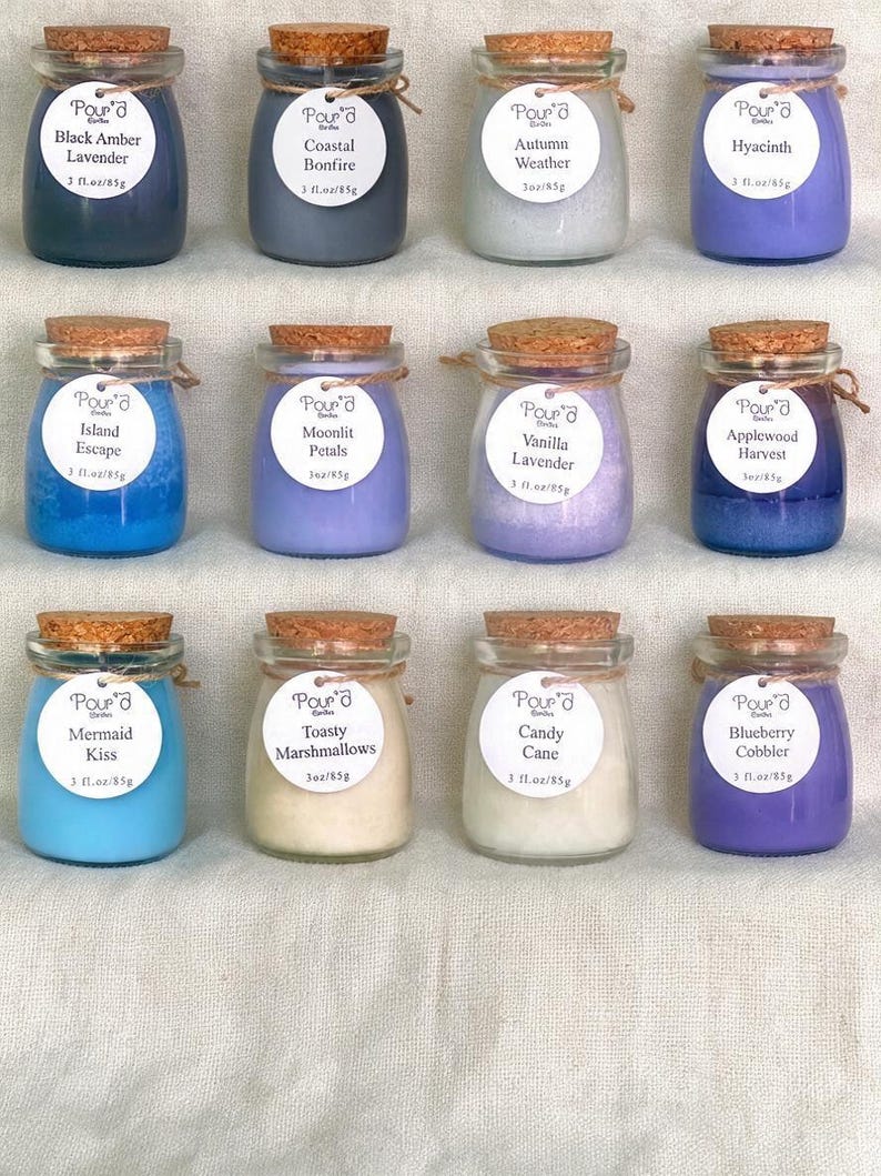 May include: Twelve small glass jars filled with colored wax candles, each topped with a cork stopper and a white circular label reading Pour'd Candles with scent names like Black Amber Lavender, Coastal Bonfire, and 3 fl. oz/85g.