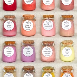 May include: Sixteen small glass jars filled with colored wax, each topped with a cork stopper. Each jar features a white circular label with the text Pour'd Earth, a scent name, and 3 fl. oz/85g. The scents include Cherry Spice, Cranberry Apple Marmalade, Rose Petals, Cranberry Grove, Frosty Berries, Orchid & Sea Salt, Fresh Picked Strawberries, Amazing Grace, Lavender Lemon, Cotton Candy, Apple Maple Bourbon, Lemon Zest, Salted Caramel Apricot, Orange & Ginger, Pumpkin Cheesecake, and Fall-tastic.