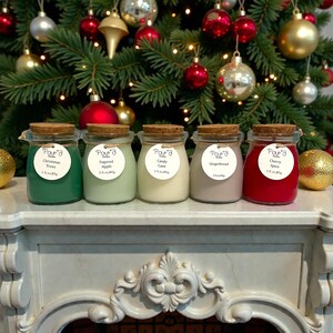 May include: Five glass jars with cork lids, each containing wax in different colors: dark green, light green, off-white, beige, and red. Each jar has a round white label with the text Pour'd Candles, a scent name, and 3 fl.oz./85g.