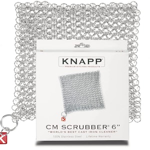 May include: A silver chainmail scrubber for cleaning cast iron cookware. The scrubber is 6 inches in size and comes in a white package with the brand name "KNAPP" and the text "CM SCRUBBER® 6" "WORLD'S BEST CAST IRON CLEANER" 100% Stainless Steel Lifetime Warranty".